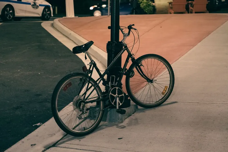 A solitary bicycle chained to a lamp post on a quiet street corner during the night