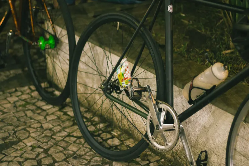 A close-up of a bicycle wheel and frame with a bottle in an urban setting at night