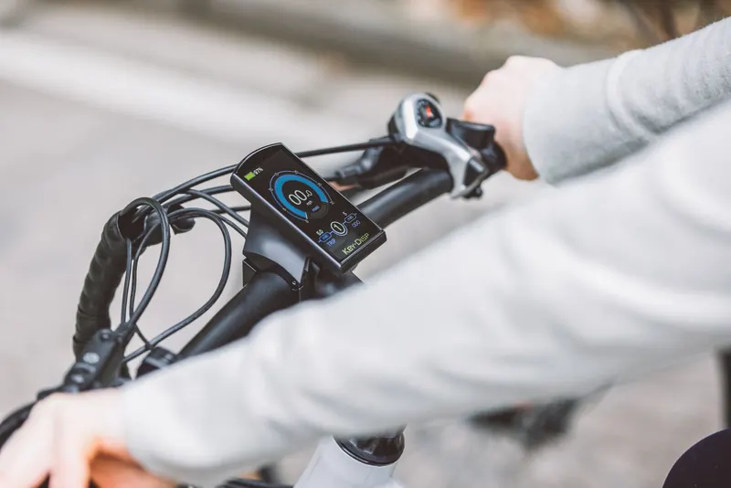 Hands gripping the handlebar of an electric bicycle, showcasing the digital display screen for speed and battery status