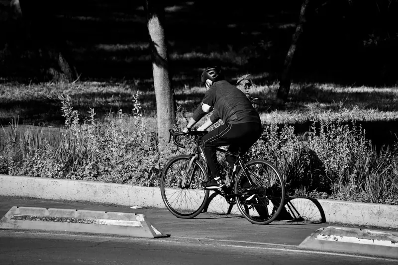 Monochrome image of a cyclist riding through an urban park bike lane