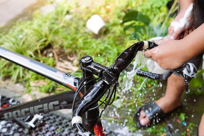Close-up of hands washing bicycle handlebars with soap and water outdoors
