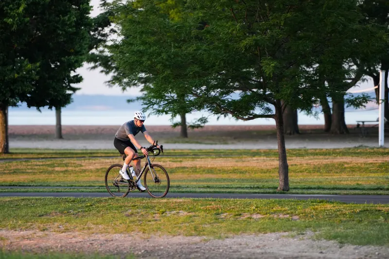 Cyclist enjoying a ride on a peaceful park path with lush greenery and distant water view