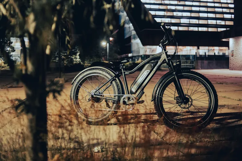 A sleek electric bike is parked on a city pavement, illuminated by streetlights at night